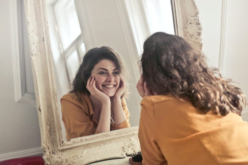 Chica sonriendo mientras se mira al espejo