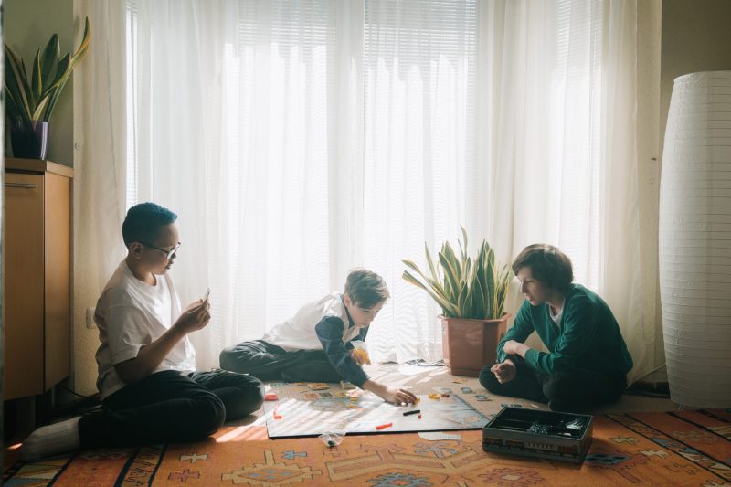 Tres chicos jugando a un juego de mesa en el suelo con una cortina blanca al fondo.
