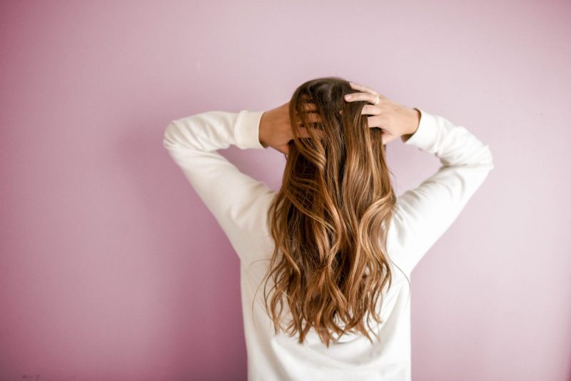 Chica de espaldas con el pelo largo castaño sobre pared rosa