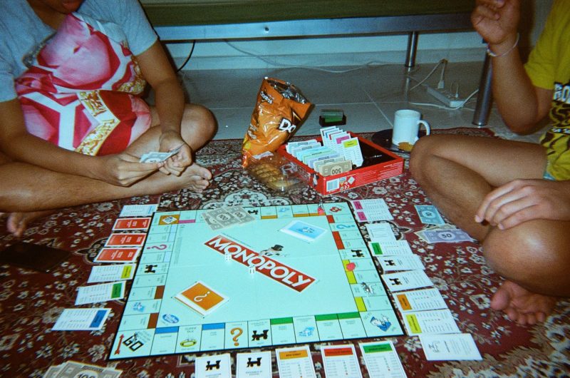 Tres amigos juegan al Monopoly sentados en una alfombra mientras comen Doritos
