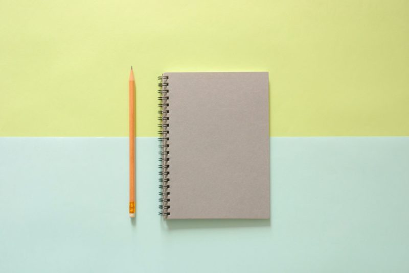 Cuaderno gris sobre un fondo verde con un lápiz amarillo