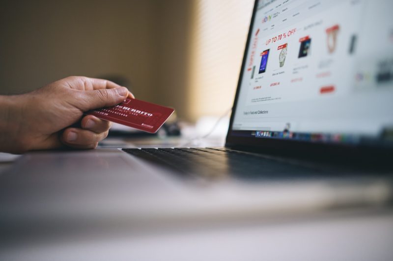 Detalle sobre una mano sosteniendo una tarjeta de crédito mientras en la pantalla se muestran compras online